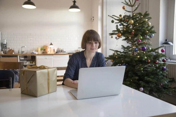 Beautiful woman using laptop while sitting at table in front of christmas tree