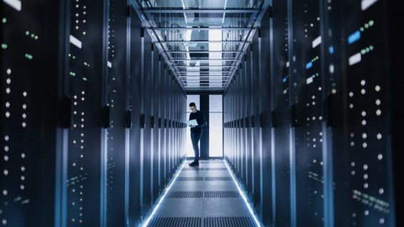 Male it engineer works on a laptop in a big data center. rows of rack servers are seen.