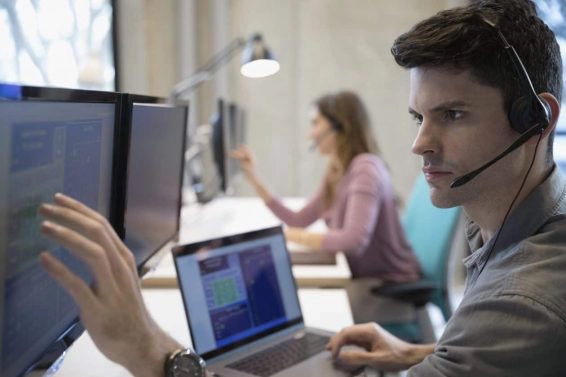 Technical support operator with headset working at laptop and computer