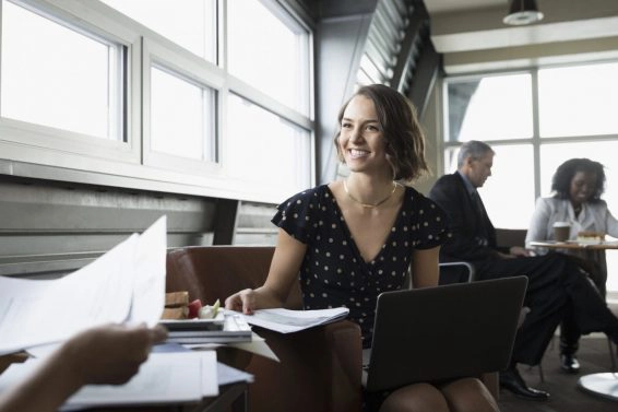 Smiling, confident businesswoman with paperwork using laptop in business lounge