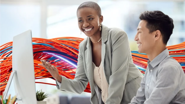 Two happy employees talking, looking at a desktop computer screen