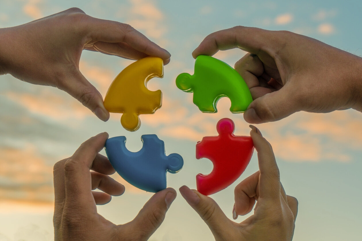 Four hands of businessmen connect colored pieces of the puzzle i