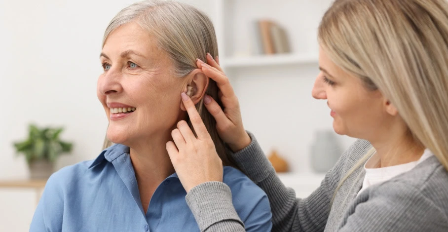 A woman helping another woman adjust her hearing aid.