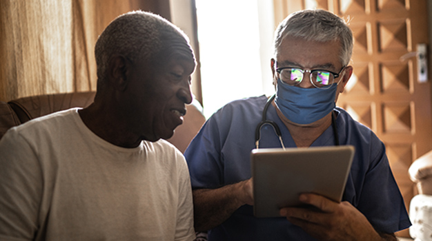 Health visitor and a senior man during home visit   using digital tablet