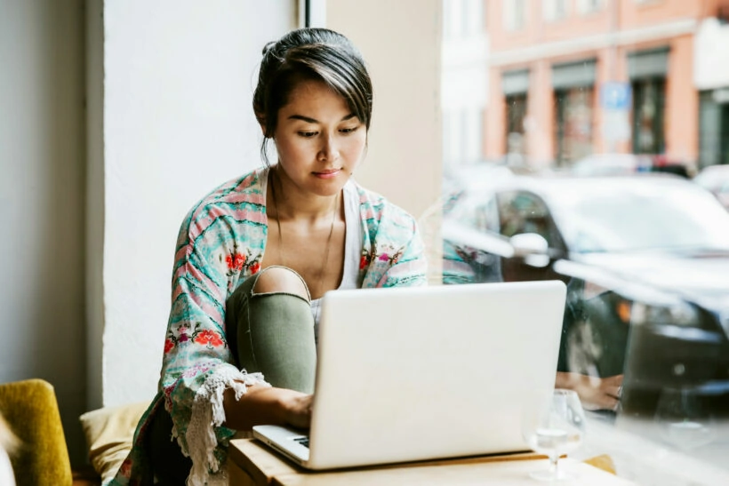 Young woman working on laptop in cafe window