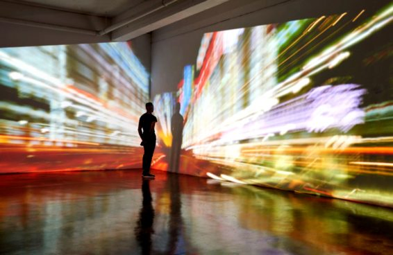 Man looking into a nighttime cityscape being projected in gallery space