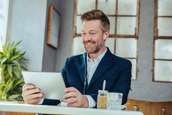 Smiling businessman with tablet and earbuds in a cafe