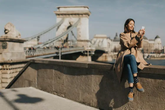 Young woman using mobile phone with chain bridge at background in budapest