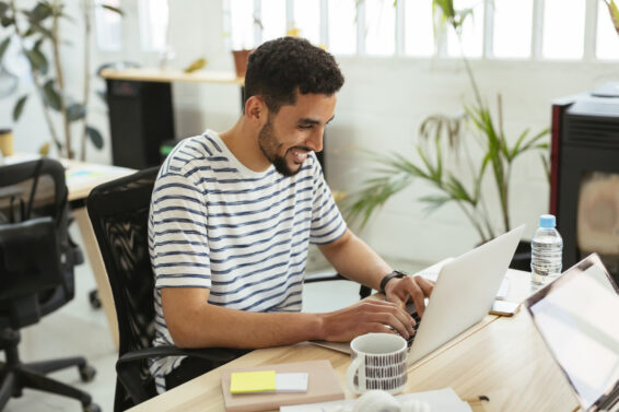 Smiling young man using laptop at desk in office