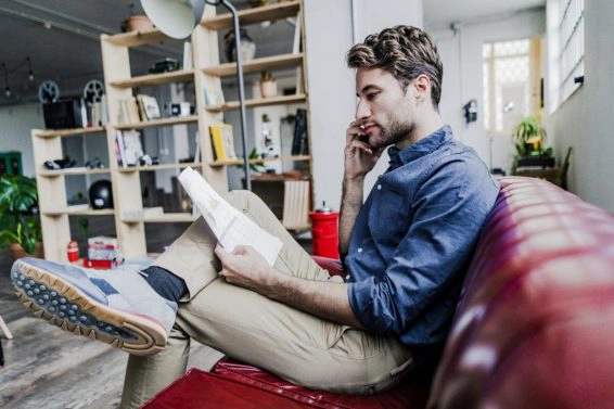Businessman holding document talking on cell phone sitting on couch in loft office