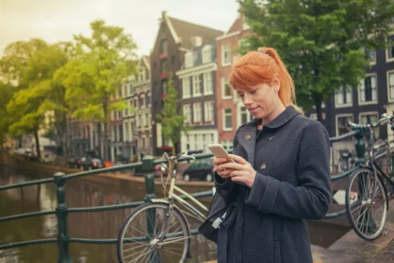 Happy girl using a smart phone in amsterdam streets