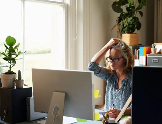 Stressed woman with hand in hair holding credit card at computer in home office