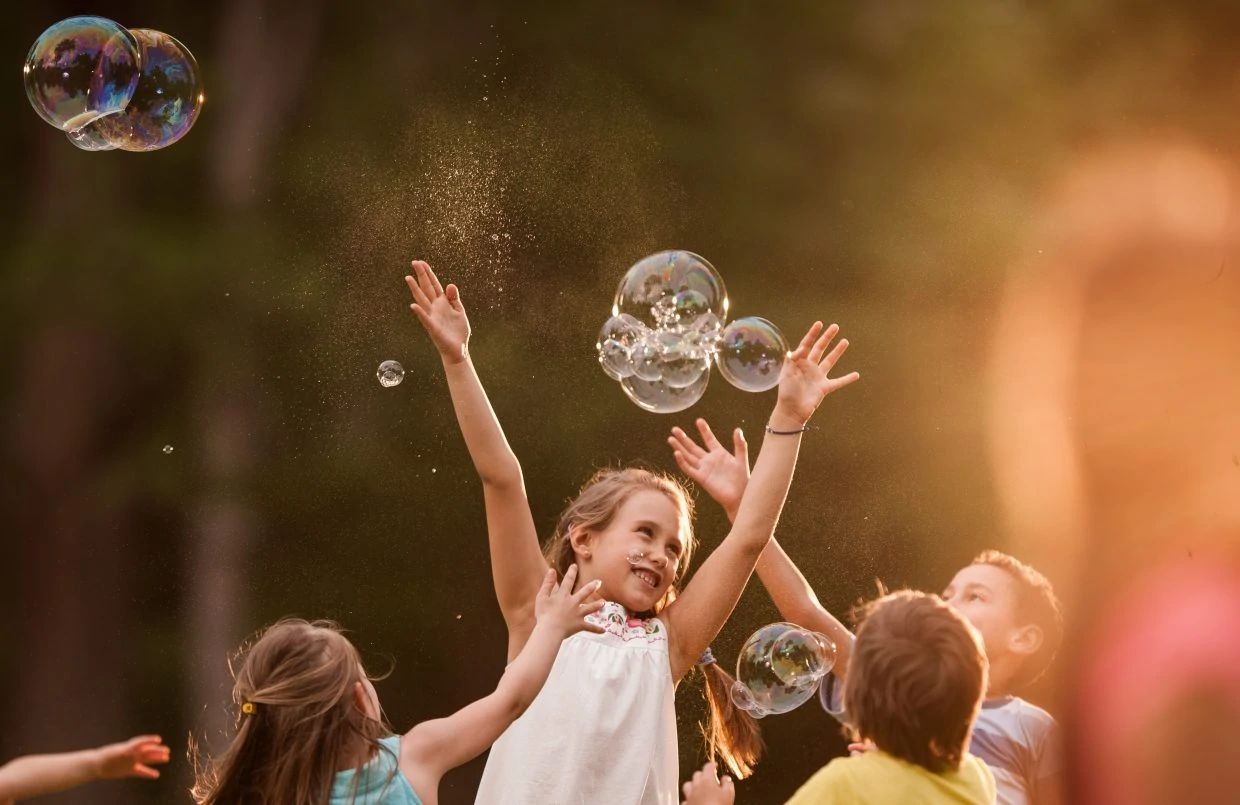 Group of kids having fun while catching rainbow bubbles in springtime.