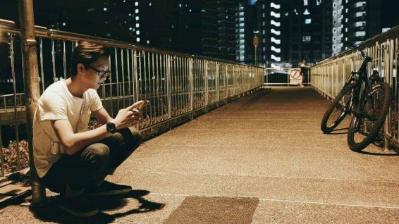 Man sitting below street light looking at mobile phone on bridge