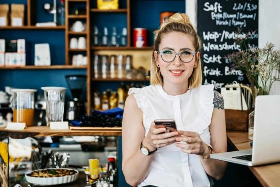 Stylish young woman smiling using smartphone in cafe”n