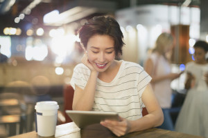 Young woman using digital tablet and drinking coffee in cafe