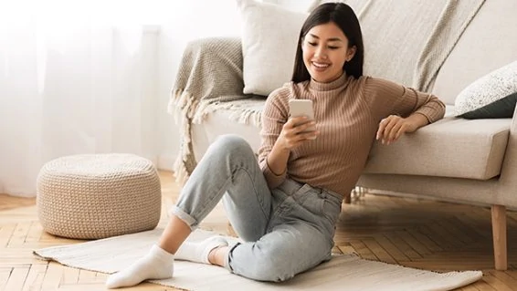 Happy asian girl messaging on phone at home