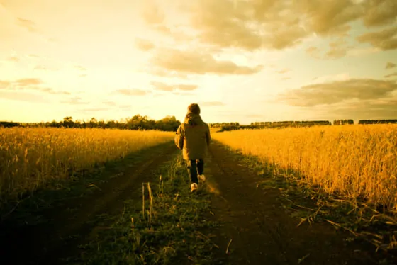 Mixed race child walking on path through rural field