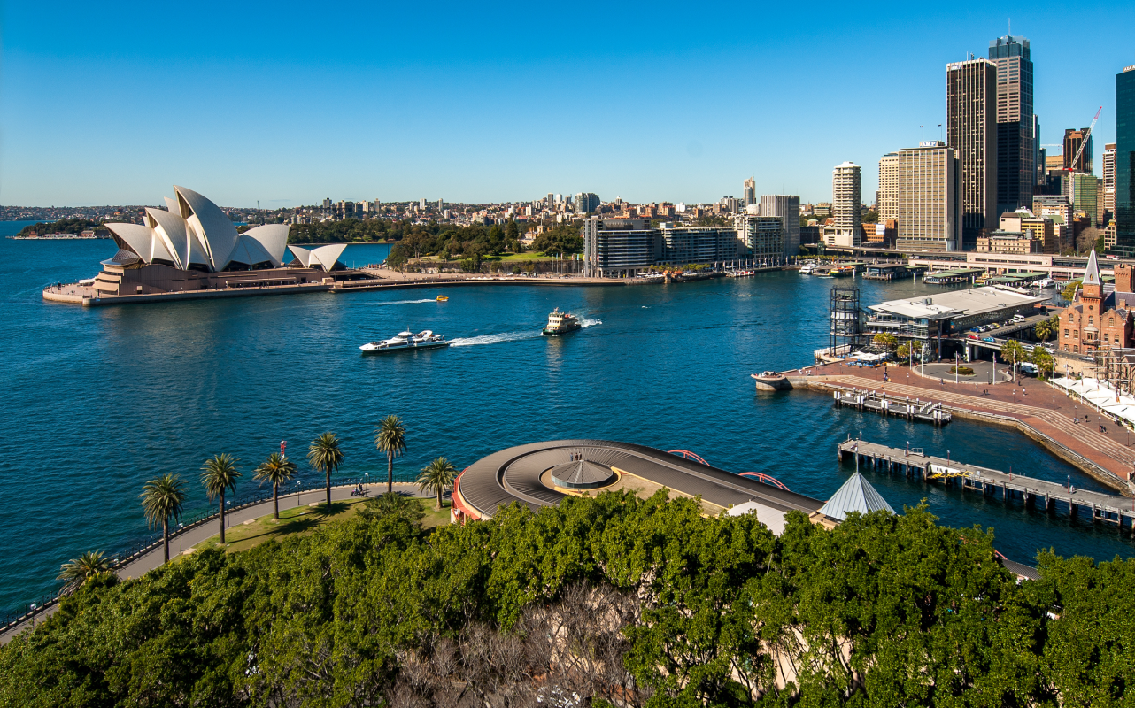 Sydney Harbour with the Opera House, ferries, and city skyline on a sunny day.